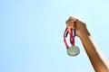 Woman hand raised, holding gold medal against sky. award and victory concept