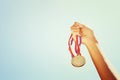 Woman hand raised, holding gold medal against sky. award and victory concept