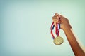 Woman hand raised, holding gold medal against sky. award and victory concept Royalty Free Stock Photo