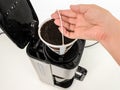 Woman hand removing mesh basket filter full of used ground coffee from drip-type coffee maker. Home electrical appliances.