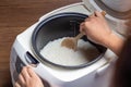 Woman hand is scooping jasmine rice cooking in electric rice cooker with steam. Thai Jasmine rice