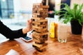 Woman hand slowly pulling wooden block from unstable Jenga blocks stacking