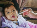 Woman hand with spoon feeding her daughter, a sweet and adorable beautiful Asian Chinese baby girl 7 or 8 months old sitting at Royalty Free Stock Photo