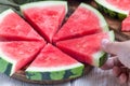 Woman hand take slice of fresh seedless watermelon cut into triangle shape laying on a wooden plate, horizontal Royalty Free Stock Photo