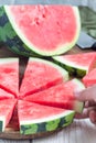 Woman hand take slice of fresh seedless watermelon cut into triangle shape laying on a wooden plate, vertical Royalty Free Stock Photo