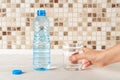 Woman hand takes a glass of pure drinking water near a half full blue plastic bottle from a white wood table. Quench thirst and Royalty Free Stock Photo