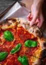 Woman Hand takes a slice of Pepperoni Pizza with Mozzarella cheese, salami, Tomatoes, pepper, Spices and Fresh Basil Royalty Free Stock Photo