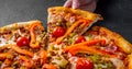 Woman Hand takes a slice of Pizza with Mozzarella cheese, Bolognese sauce, minced meat, pepper, tomato, bacon and vegetables Royalty Free Stock Photo