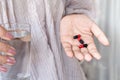 Woman hand taking antibiotic pills red and black capsules with glass of water Royalty Free Stock Photo