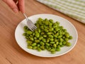 Woman hand taking green Edamame soy beans from a plate with a fork Royalty Free Stock Photo