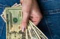 Woman hand taking money from jeans back pocket. Woman hiding money behind her back. Dollar banknotes close up