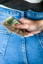 Woman hand taking money from jeans back pocket. Woman hiding money behind her back. Dollar banknotes close up