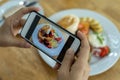 Woman hand is taking a picture of a strawberry pancake with a smartphone. Women are taking photos to post or share popular dishes