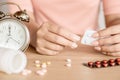 Woman hand taking pills with alarm clock on desk
