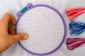 Woman hand taking plastic embroidery hoop with cross stitch fabric and some colour threads near