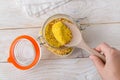 Woman hand taking universal seasoning with large wooden spoon from clip top glass jar on a white wooden kitchen table. Seasoning