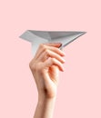 Woman hand throwing origami plane on pink background. Symbol of childhood, freedom, imagination, creativity. Paper