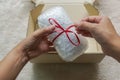 Woman hand tie a red ribbon on gift wrapped with bubble sheet before putting into carton for parcel Royalty Free Stock Photo
