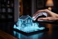 Woman hand touching virtual miniature classic house model in a meeting placed on a table, illuminated with blue neon lights. Real