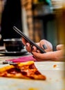 Woman hand using mobile phone in cafe with a piece of pizza in plate Royalty Free Stock Photo