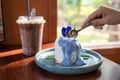 Woman hand using spoon cutting coconut cake with butterfly pea topping on ceramic dish and iced cocoa on the table