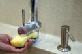 Woman hand washes chrome plated water faucet with yellow sponge in new modern kitchen. Liquid soap dispenser with Royalty Free Stock Photo