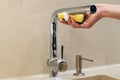 Woman hand washes chrome plated water faucet with yellow sponge in new modern kitchen. Liquid soap dispenser with Royalty Free Stock Photo