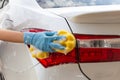 Woman hand wearing blue gloves with yellow sponge washing taillight modern car or cleaning automobile. Royalty Free Stock Photo