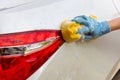 Woman hand wearing blue gloves with yellow sponge washing taillight modern car or cleaning automobile. Royalty Free Stock Photo