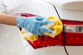 Woman hand wearing blue gloves with yellow sponge washing taillight modern car or cleaning automobile. Royalty Free Stock Photo