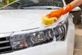 Woman hand wearing orange gloves with yellow sponge washing headlight modern car or cleaning automobile.