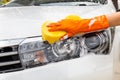 Woman hand wearing orange gloves with yellow sponge washing headlight modern car or cleaning automobile.