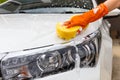 Woman hand wearing orange gloves with yellow sponge washing headlight modern car or cleaning automobile.