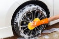 Woman hand wearing orange gloves with yellow sponge washing wheel modern car or cleaning automobile. Royalty Free Stock Photo