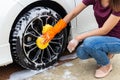 Woman hand wearing orange gloves with yellow sponge washing wheel modern car or cleaning automobile. Royalty Free Stock Photo