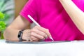 Woman hand with wristwatch in bright T-shirt sits at table tablet, pencil hands