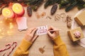 Woman hand writing a Christmas greeting card on a wooden background. Merry Xmas rustic decor stuff and winter holiday concept in Royalty Free Stock Photo