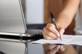 Woman hand writing a contract with a laptop beside