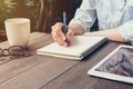 Woman hand writing note pad on wood table in coffee shop. Royalty Free Stock Photo