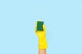 Woman hand with yellow rubber glove holding a cleaning sponge on a light blue background Royalty Free Stock Photo