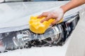 Woman hand with yellow sponge washing headlight modern car or cleaning automobile.