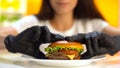 Woman hands in black rubber gloves taking fat double burger from white plate