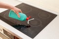 Woman hands with bottle of cleaning detergent for induction stove applies a scour to the burner. House cleaning.