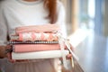 Woman hands carrying stylish designed coral and white coloured stack of diaries with gold pen.