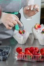 Woman hands chef decorating Cupcakes with pink butter cream and fresh berries in white baking parchment cases Royalty Free Stock Photo