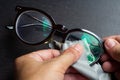 Woman hands cleaning shortsighted or nearsighted eyeglasses by microfibre cleaning cloths, On black background, Optical concept