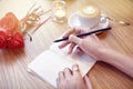 Woman hands close-up writing in notebook, using pencil, blank pages for layout. Cappuccino latte coffee with heart on top. Flowers Royalty Free Stock Photo