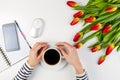 Woman hands with cup of coffee and computer mouse. Mobile phone, paper notebook and beautiful tulips on white table Royalty Free Stock Photo