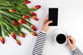 Woman hands with cup of coffee, mobile phone and beautiful flowers bunch on the white office table Royalty Free Stock Photo