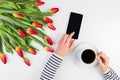 Woman hands with cup of coffee, mobile phone and beautiful flowers bunch on the white office table Royalty Free Stock Photo